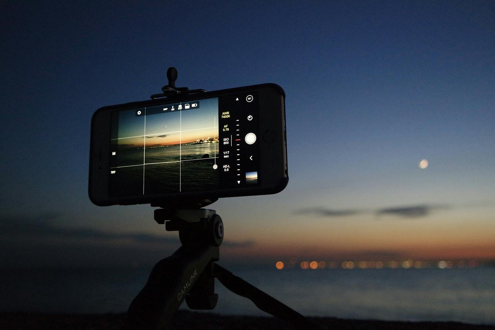 An evening scene of a smartphone on a tripod taking a photo of the sunset over the ocean.